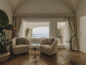A room with two armchairs, a small round table, and a large window with curtains.