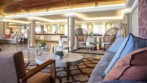 Un hallo espacioso con techos altos, una zona de estar central con sofás y sillones, y un mostrador de recepción al fondo.