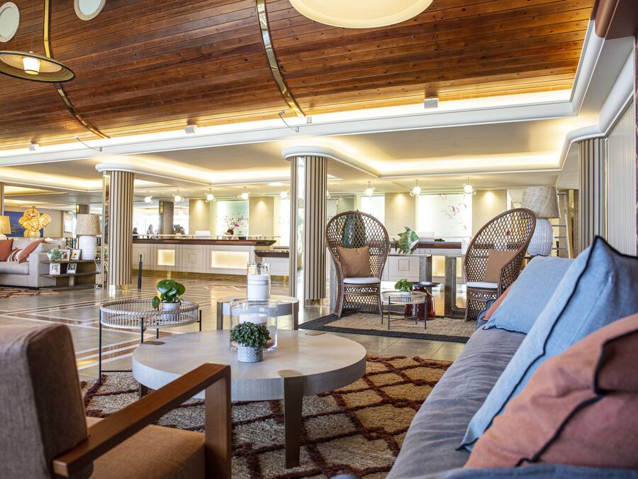 A spacious lobby with a high ceiling, a central seating area with sofas and chairs, and a reception desk in the background.
