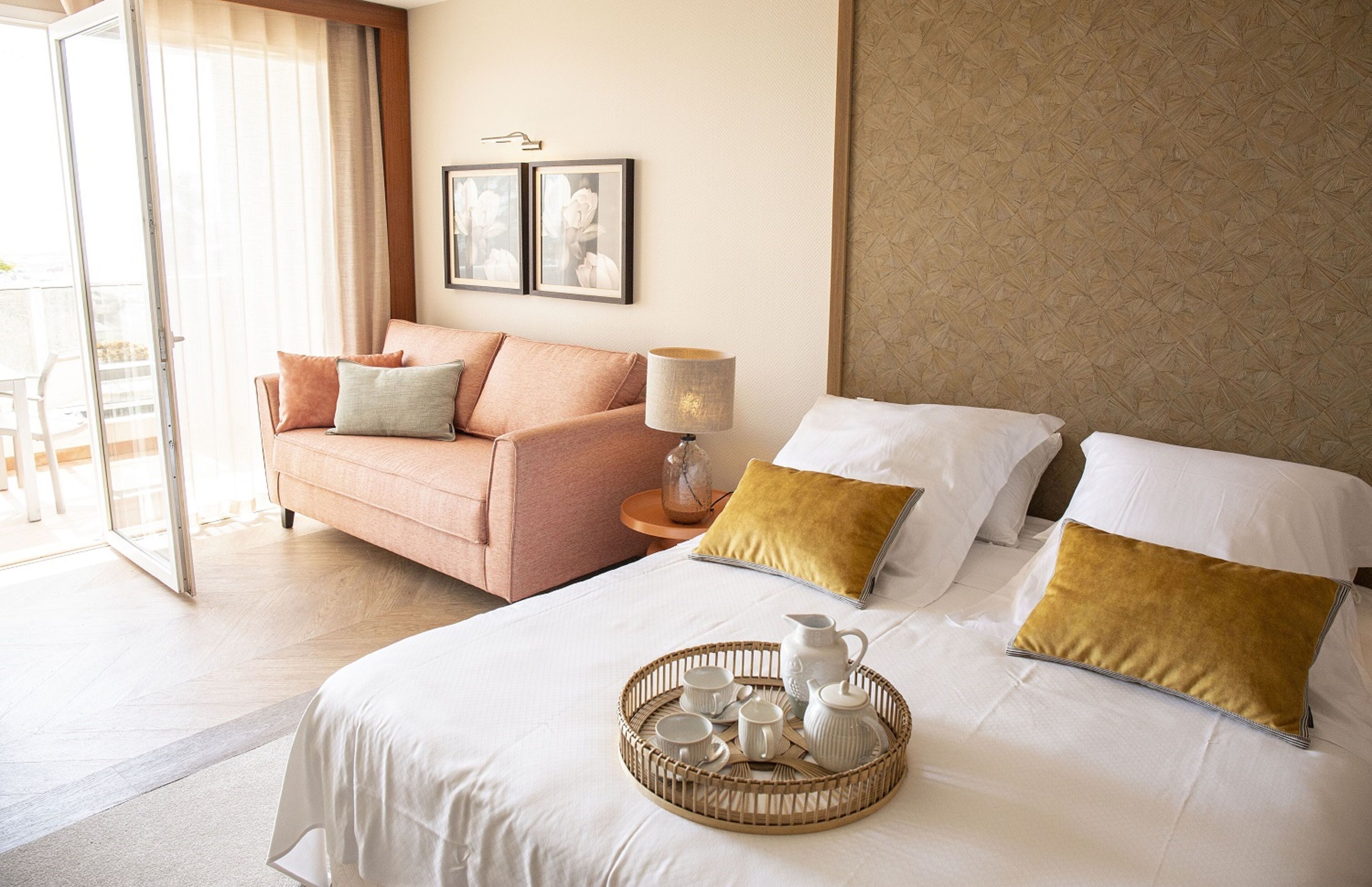 A hotel room with a bed, a sofa, and a dining area with a tray of tea set.