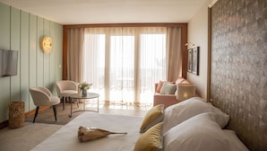 Una habitación de hotel con una cama, dos sillones, una mesita y un ventanal con cortinas.