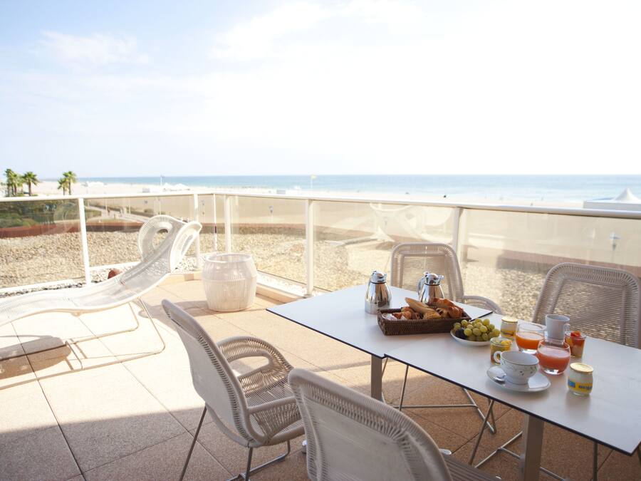 Un balcon avec une table dressée pour le petit-déjeuner, donnant sur une plage.