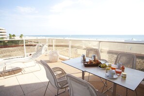 A balcony with a table set for breakfast, overlooking a beach.