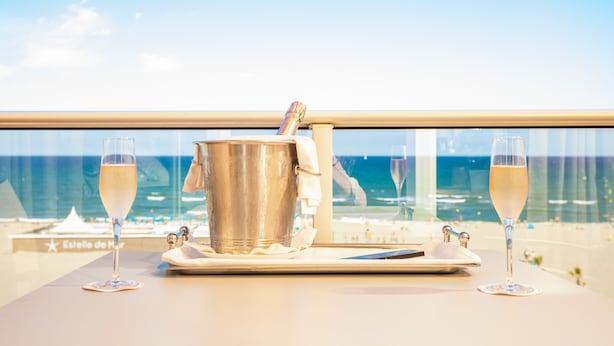 Una mesa con un cubo de champán y dos copas, con vistas a una playa y un cielo despejado.