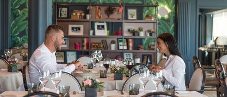 A dining area with tables set for two, each with wine glasses and floral centerpieces.
