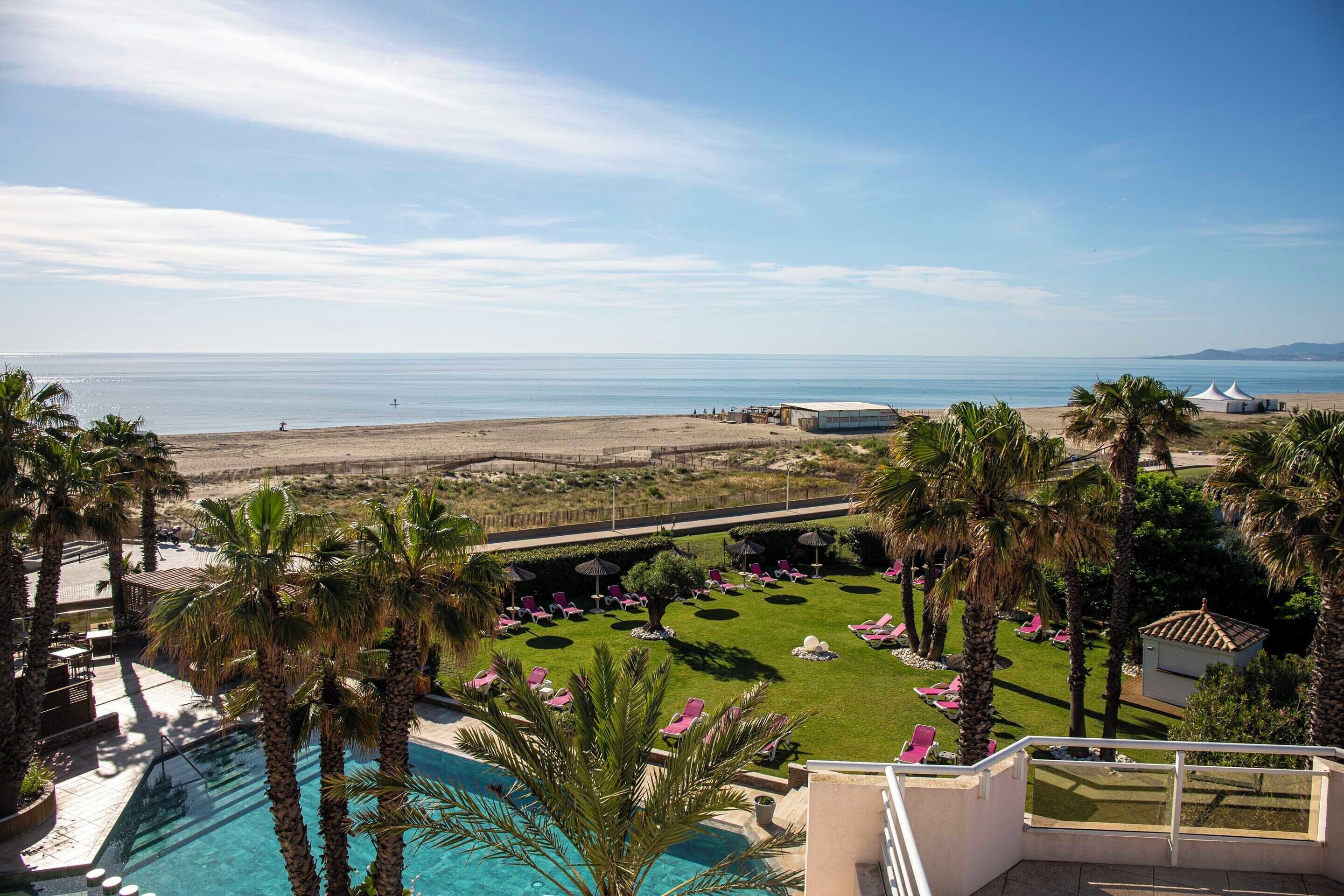 Un complexe hôtelier doté d’une piscine, de palmiers et offrant une vue sur la plage.