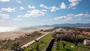 Un paisaje costero con playa, camino y zona verde con palmeras.