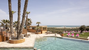 Un área de piscina con vista despejada al océano, rodeada de palmeras y sillones de descanso.