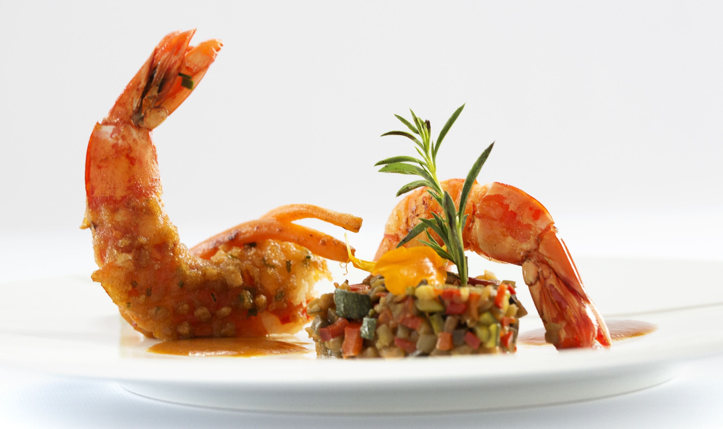 Un plat amb dues gambes cuites, una barreja petita de verdures i una branca de romaní.