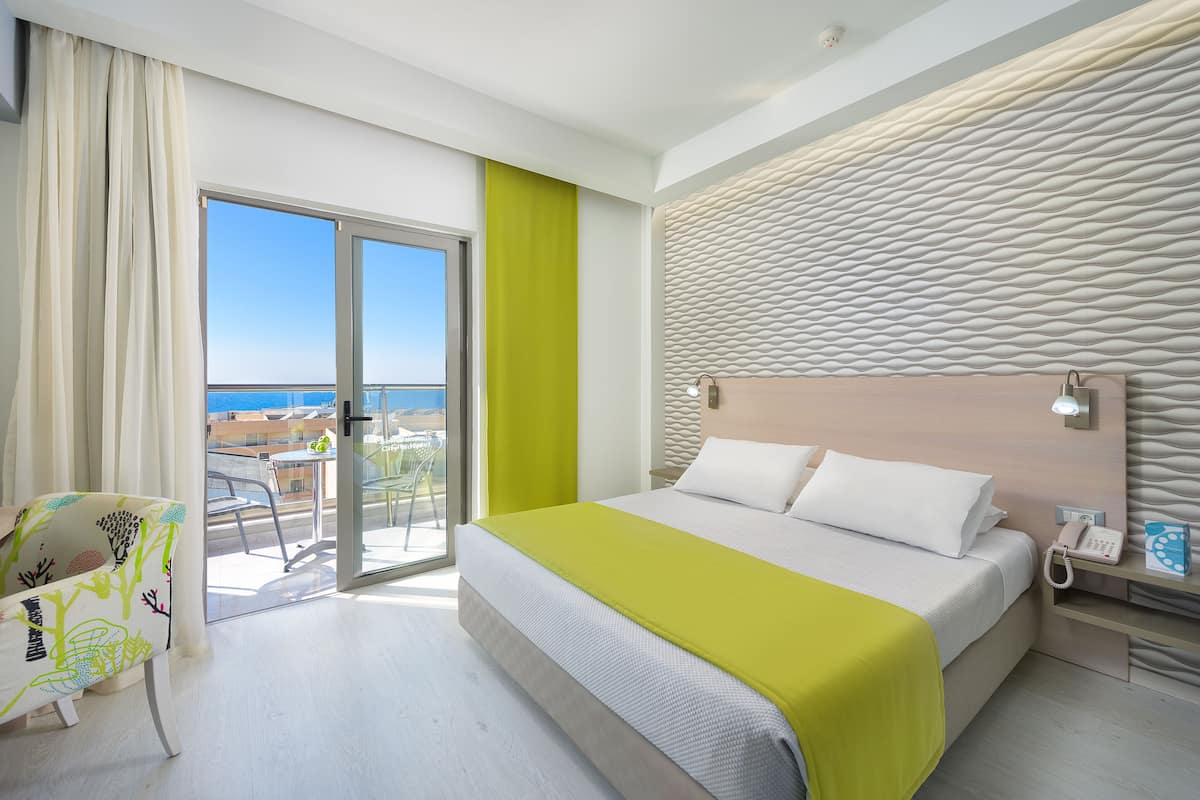 A modern hotel room with a large bed, a balcony with a view, and a bright green accent wall.