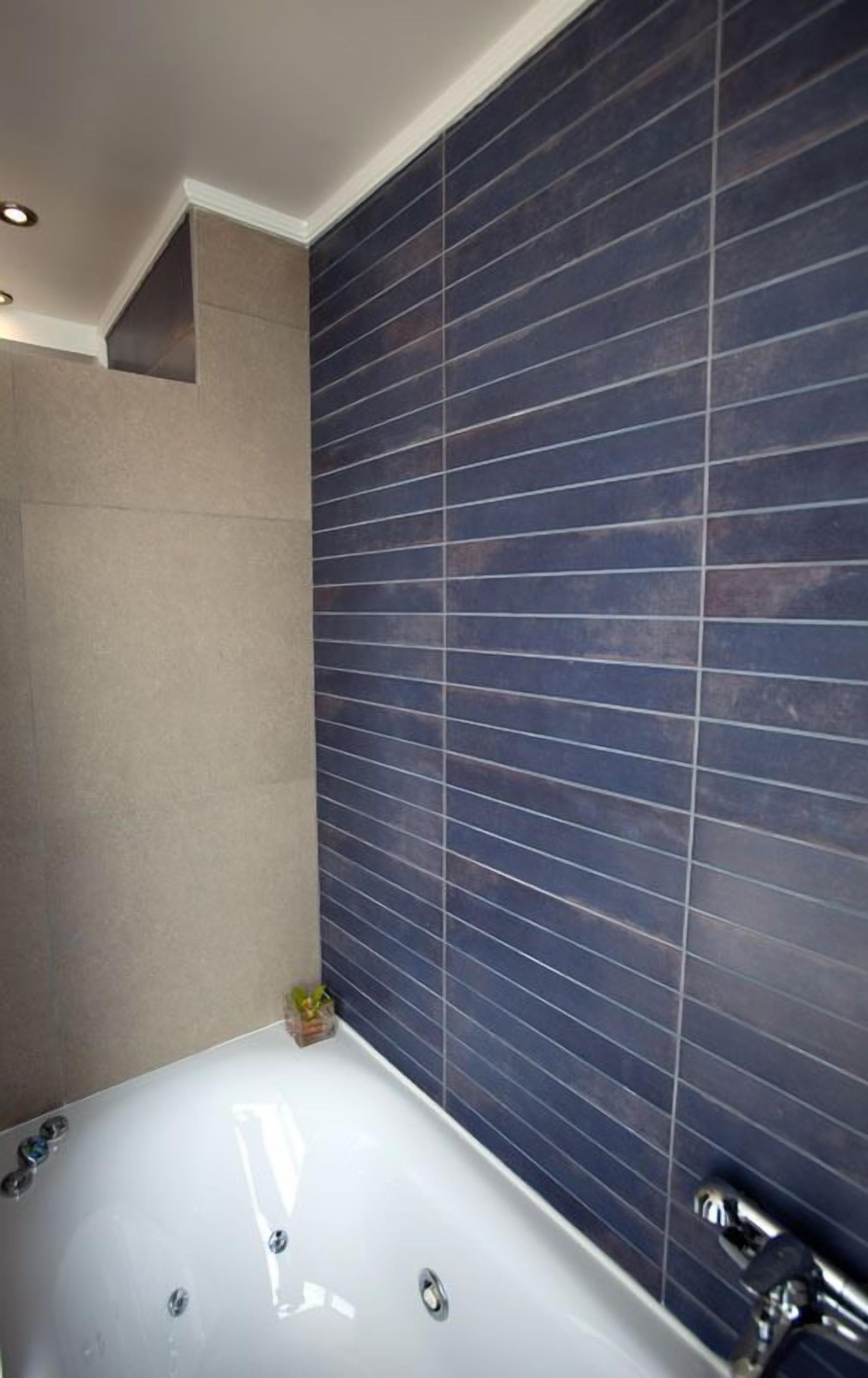 Un baño moderno con una bañera grande, paredes cubiertas de azulejos azul oscuro y suelo color beige.