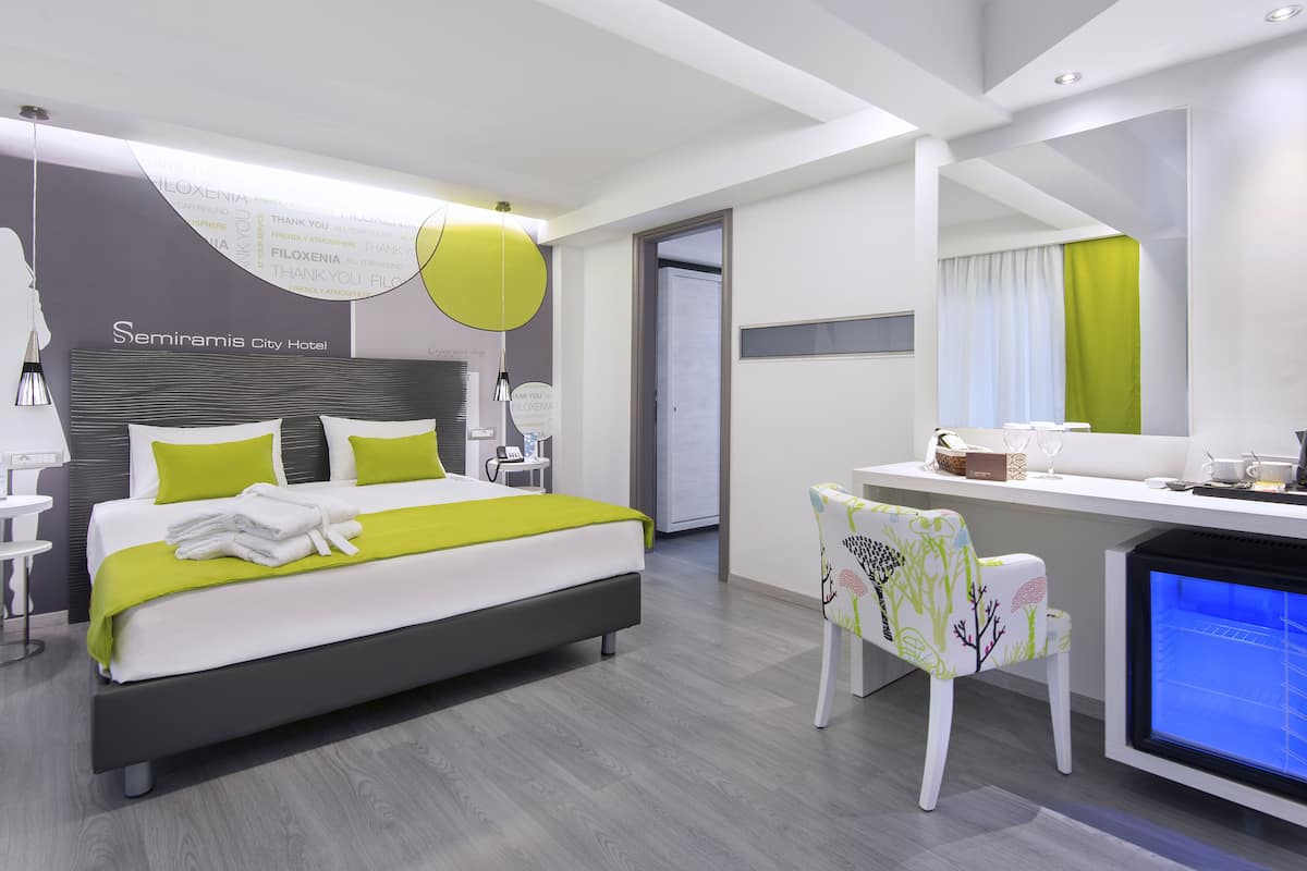 A modern hotel room with a large bed, a desk with a computer, and a small seating area.