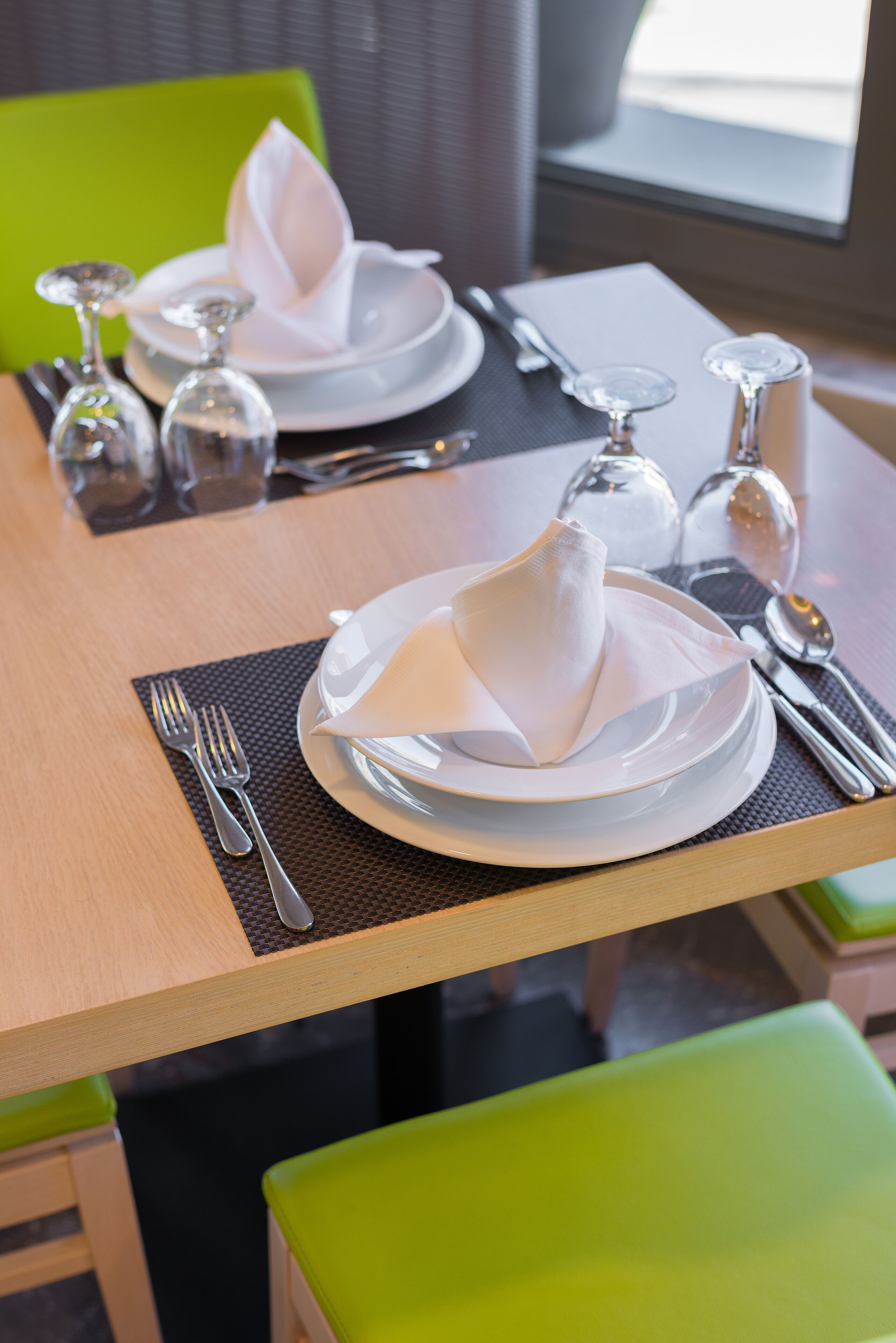 A dining table set with plates, cutlery, and glasses, with a green chair visible.