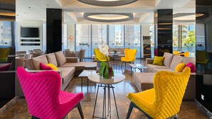 En moderne hotellobby med siddeområde, store vinduer og et fladskærms-tv på væggen.