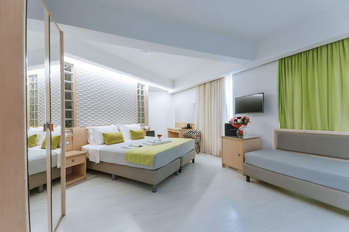 A modern hotel room with a large bed, a sofa, a TV, and a window with curtains.