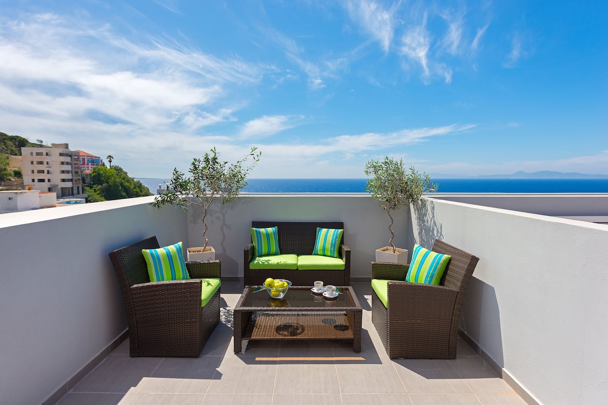 A rooftop terrace with wicker furniture, a glass coffee table, and potted plants.