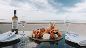 Et bord med en vinflaske, glas og et udvalg af oste samt frugt på en balkon med udsigt over havet.