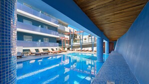 En pool med liggestole og en moderne bygning med altaner i baggrunden.