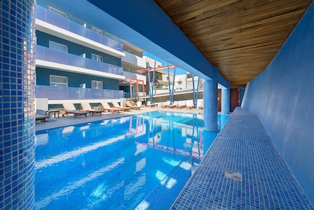 Una piscina al aire libre, sombrillas, sillones reclinables de piscina