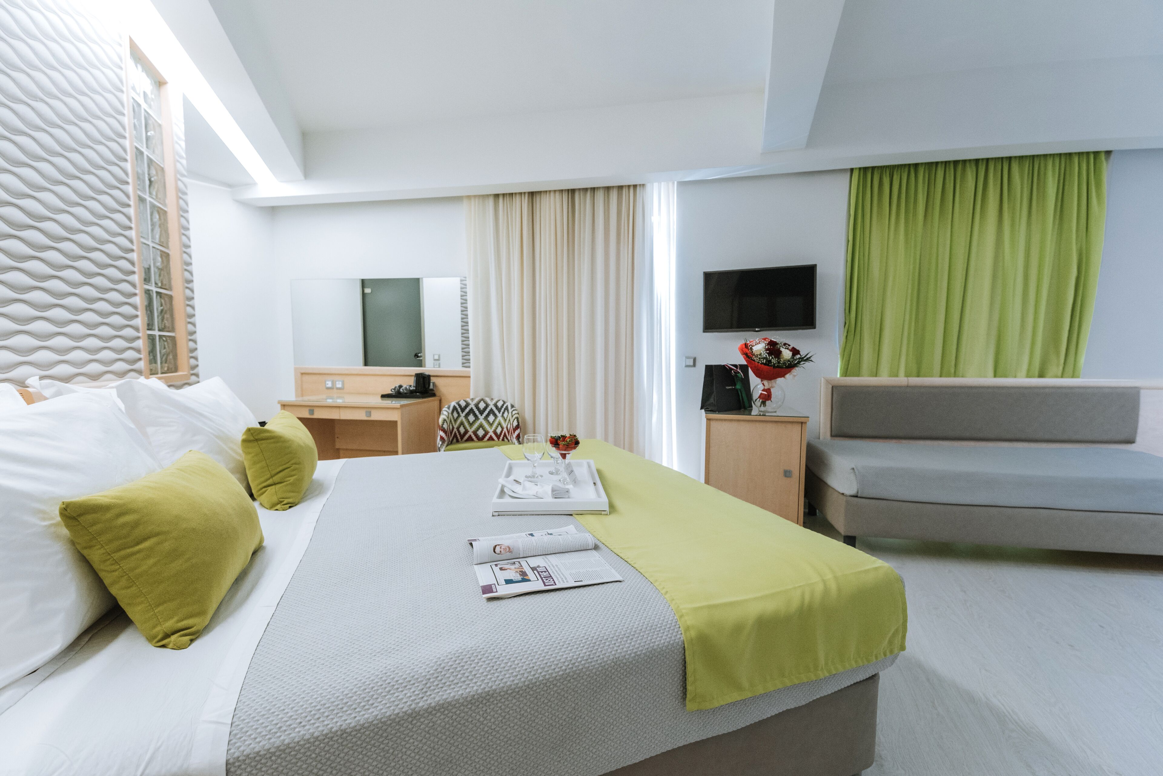 Habitació d'hotel moderna amb un llit ben arropat, un escriptori amb un ordinador, una televisió i un sofà.
