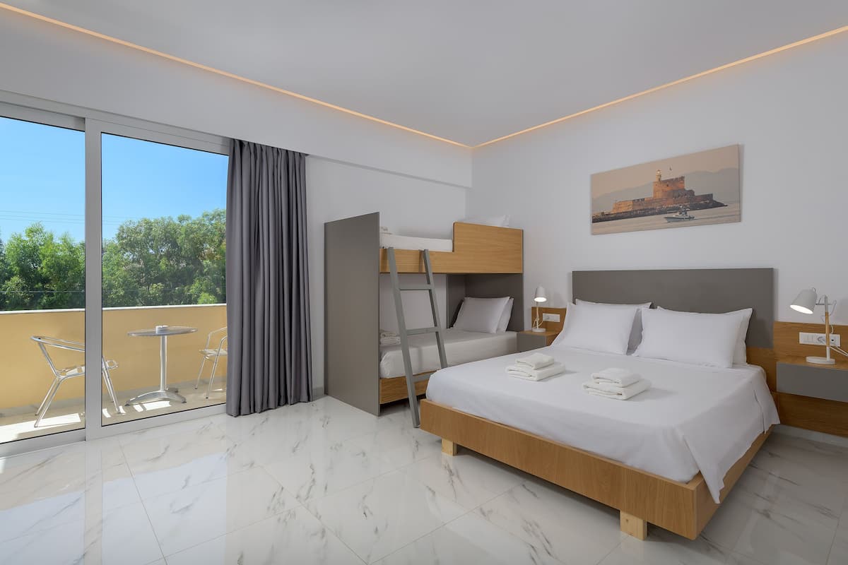 A modern hotel room with a large bed, a smaller bunk bed, a balcony with a table and chairs, and a painting on the wall.