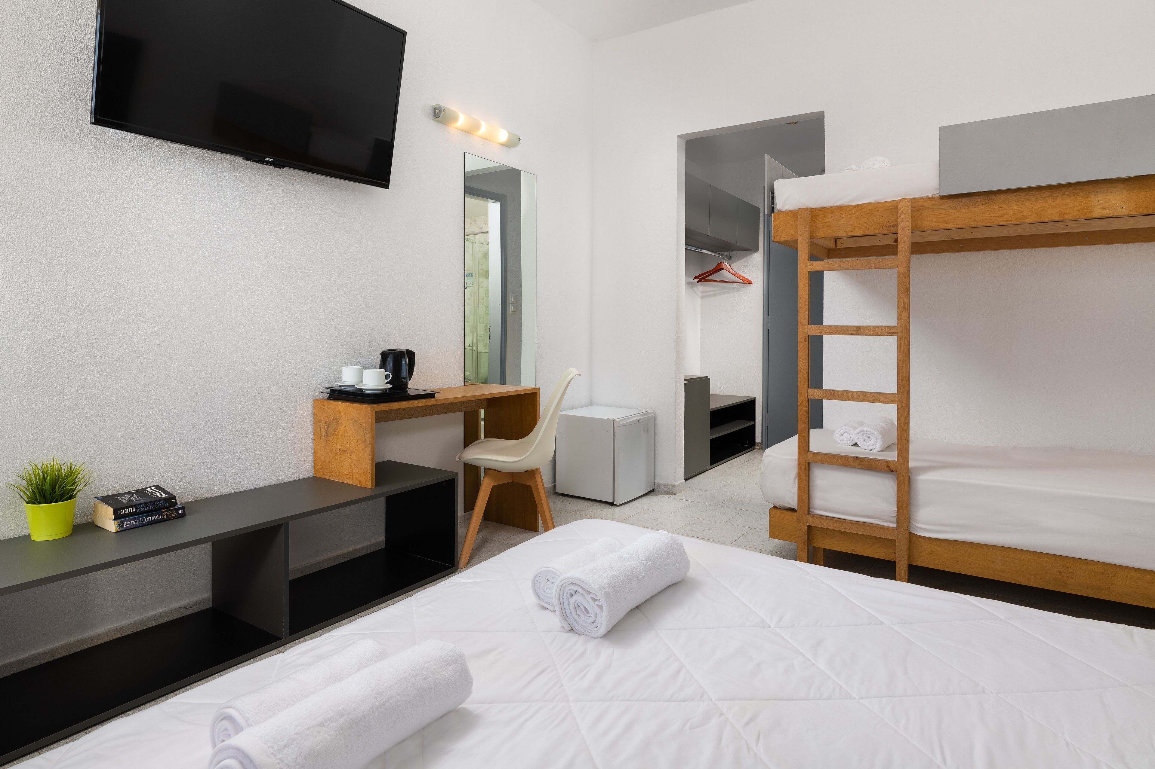 A modern hotel room with a bunk bed, a desk with a chair, a television, and a small plant.