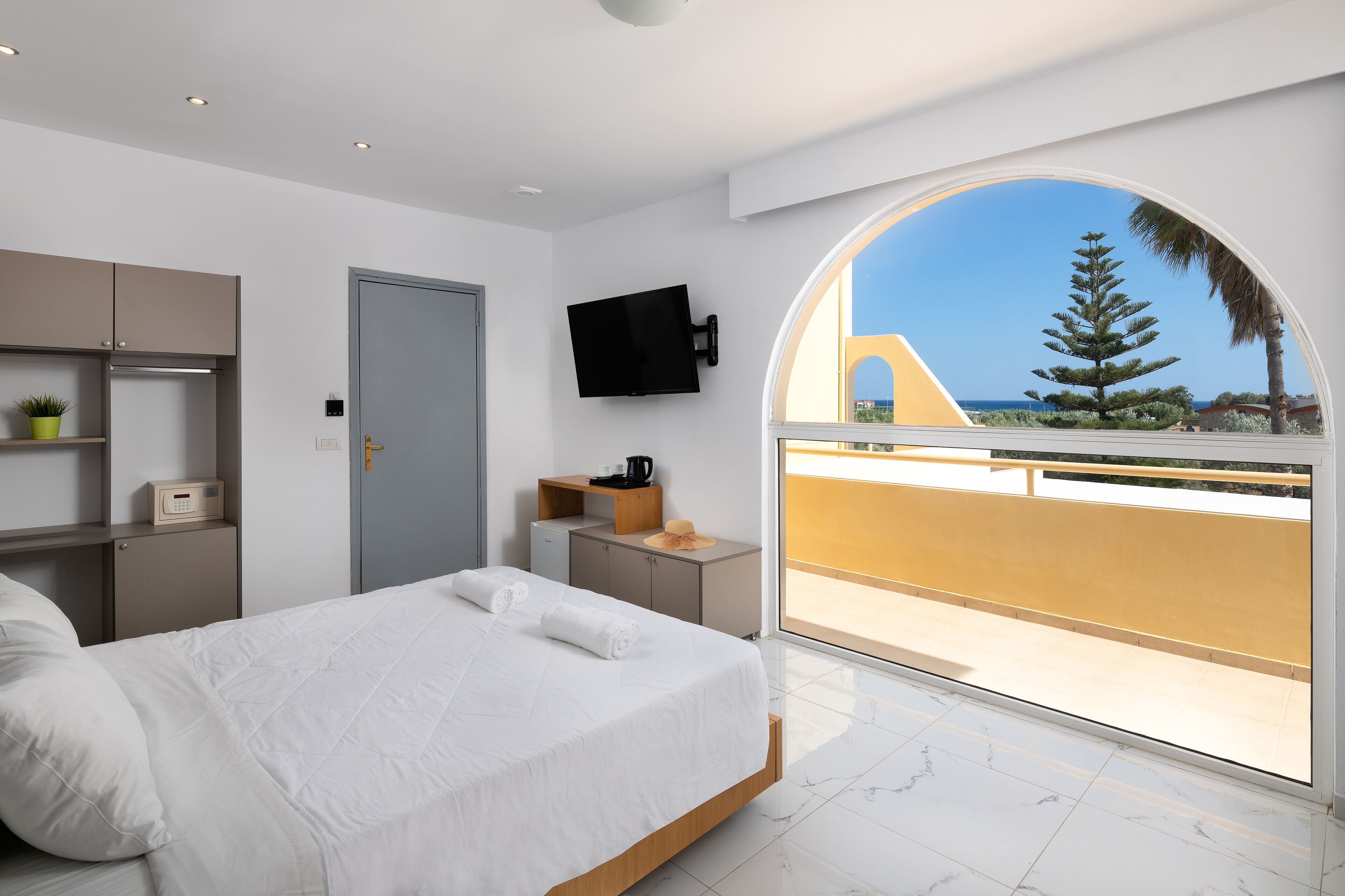 Un dormitorio moderno con una cama grande, un televisor montado en la pared y un balcón con vistas al mar.