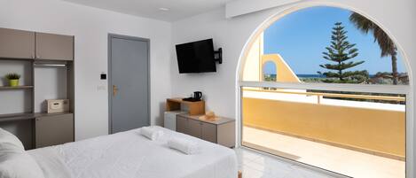 Un dormitorio moderno con una cama grande, un televisor montado en la pared y un balcón con vistas al mar.