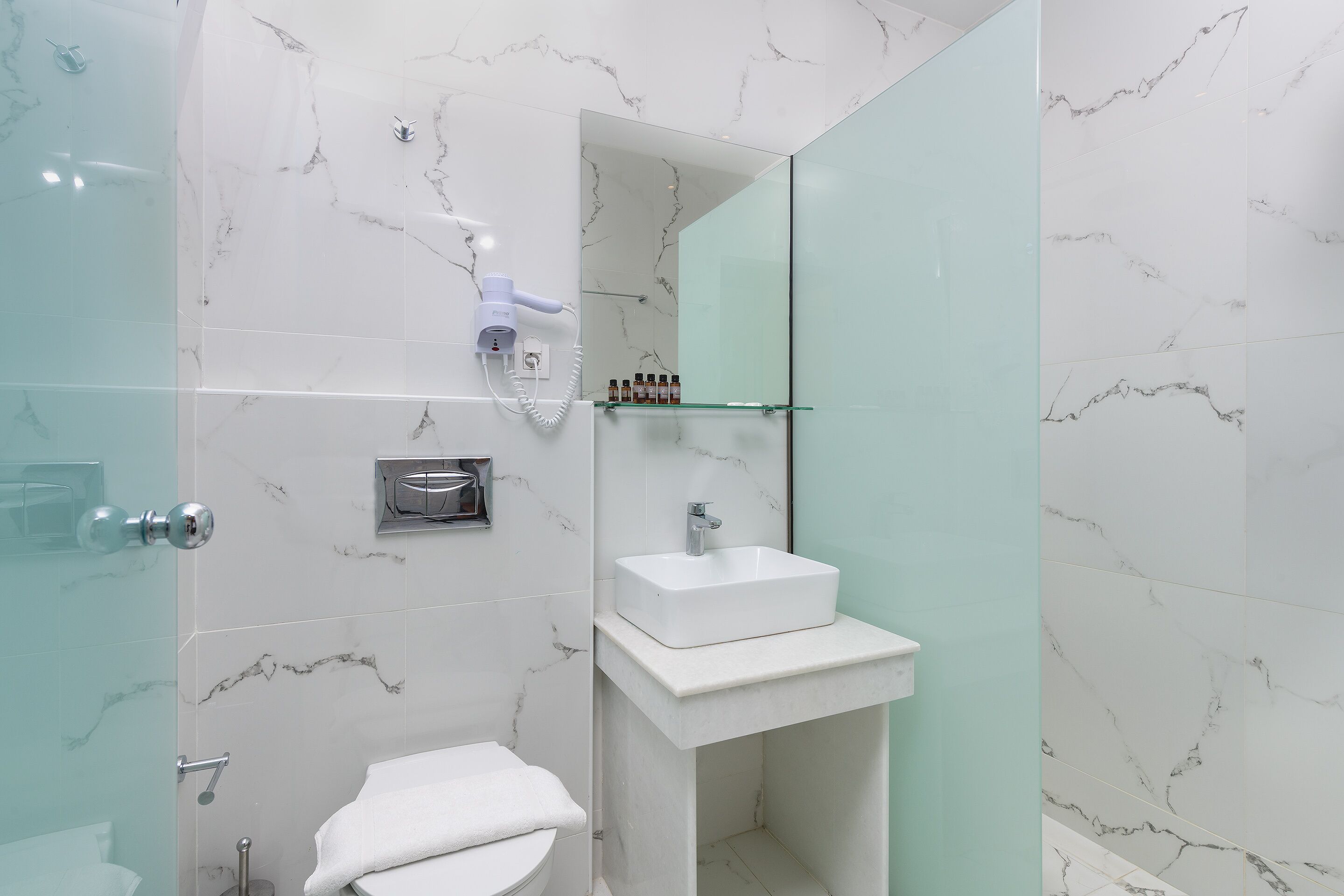 Un baño moderno con cabina de ducha de vidrio, un lavamanos blanco y un salpicadero de mármol.