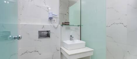 Un baño moderno con cabina de ducha de vidrio, un lavamanos blanco y un salpicadero de mármol.