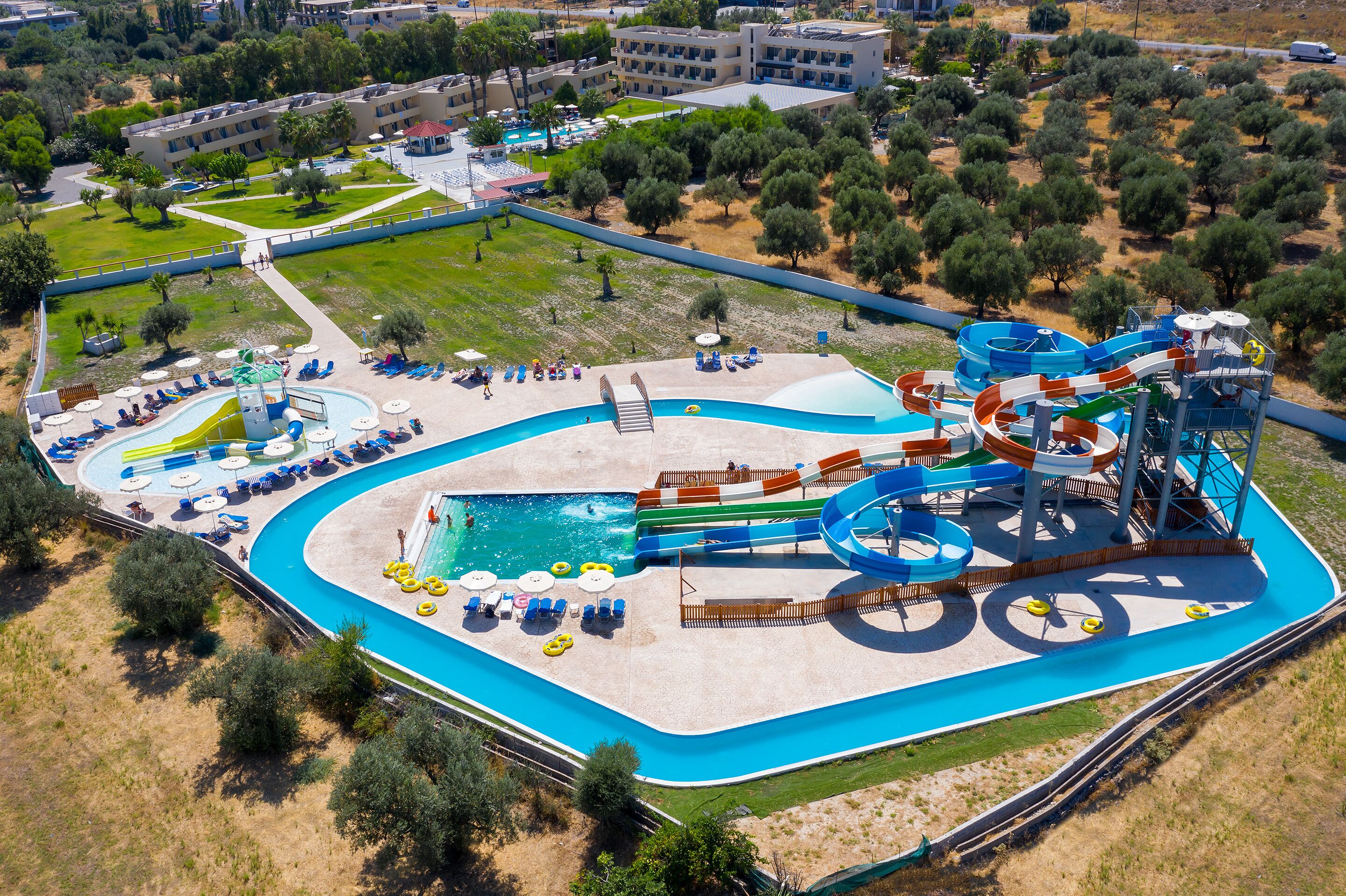 Eine Vogelperspektive eines Wasserparks mit einem großen Schwimmbecken, mehreren Wasserrutschen und Liegestühlen.