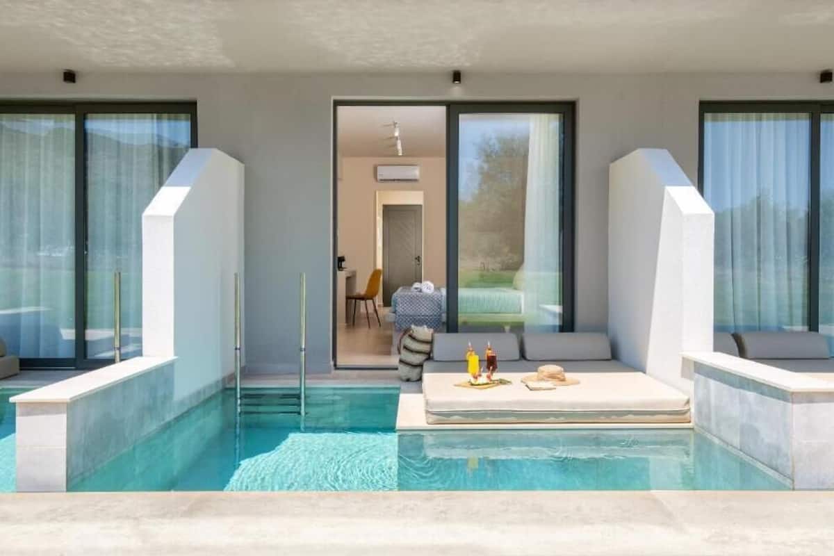 A modern outdoor pool area with a sofa and a table, large windows, and a door leading to an indoor space.