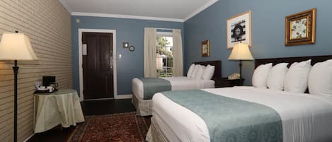 Habitación de hotel con dos camas, un tapete rojo y blanco estampado, una puerta de madera y una ventana con cortinas.