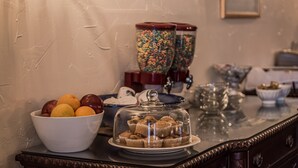 A buffet table with a bowl of fruit, a glass container with colorful beads, and a glass dome covering cupcakes.