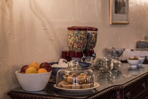 A buffet table with a bowl of fruit, a glass container with colorful beads, and a glass dome covering cupcakes.