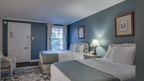 A bedroom with two beds, a window with curtains, a chair, and a nightstand with a lamp.