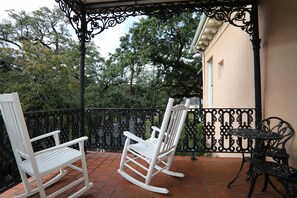 A covered patio with white rocking chairs and a small table, surrounded by a black wrought iron fence.