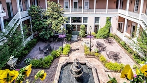 A courtyard with a central fountain, surrounded by brick pathways, outdoor seating, and lush greenery.