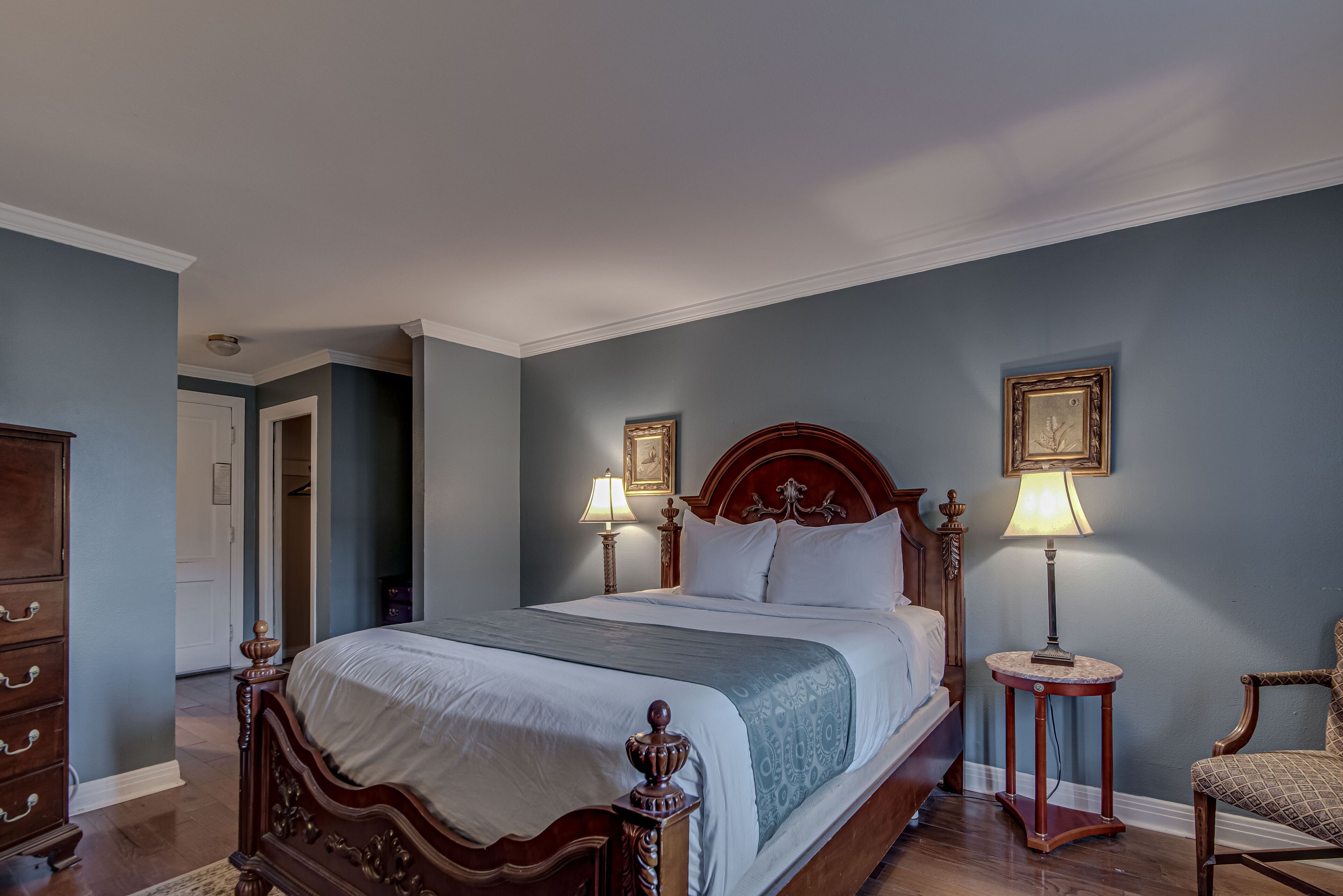 A bedroom with a wooden bed, two bedside tables with lamps, a chair, and a dresser.