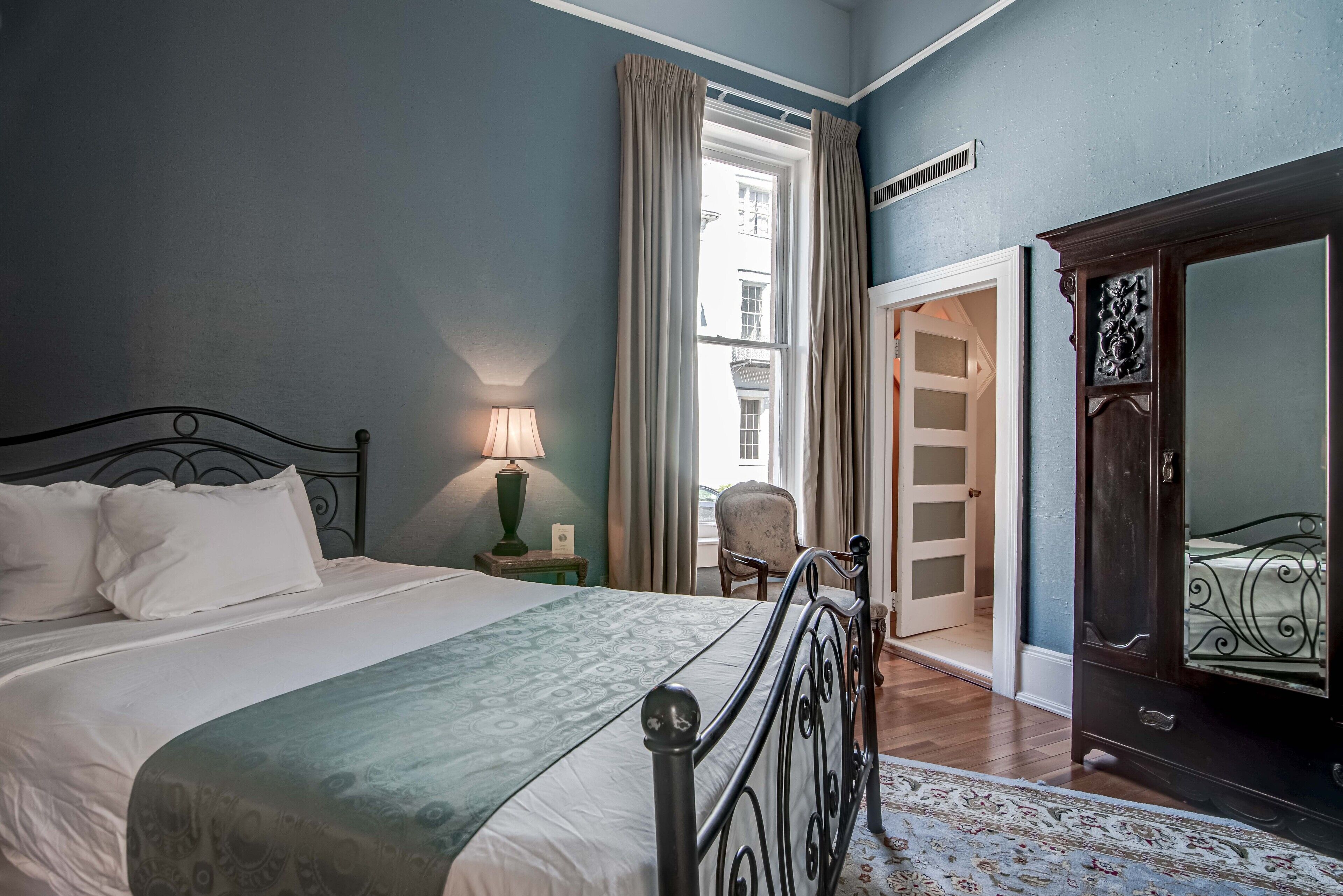 A bedroom with a bed, a chair, a wardrobe, and a window with curtains.
