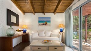 A modern living room with a wooden ceiling, a white sofa, two lamps, a glass coffee table, and a painting of a beach scene. - Dionysos Hotel (Rhodes)