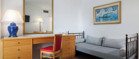 A bedroom with a wooden desk, a red chair, a bed with striped bedding, a large mirror, and a framed picture on the wall.