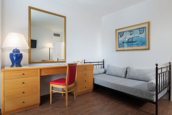 Un dormitorio con un escritorio de madera, una silla roja, una cama con ropa de cama a rayas, un espejo grande y un cuadro enmarcado en la pared.