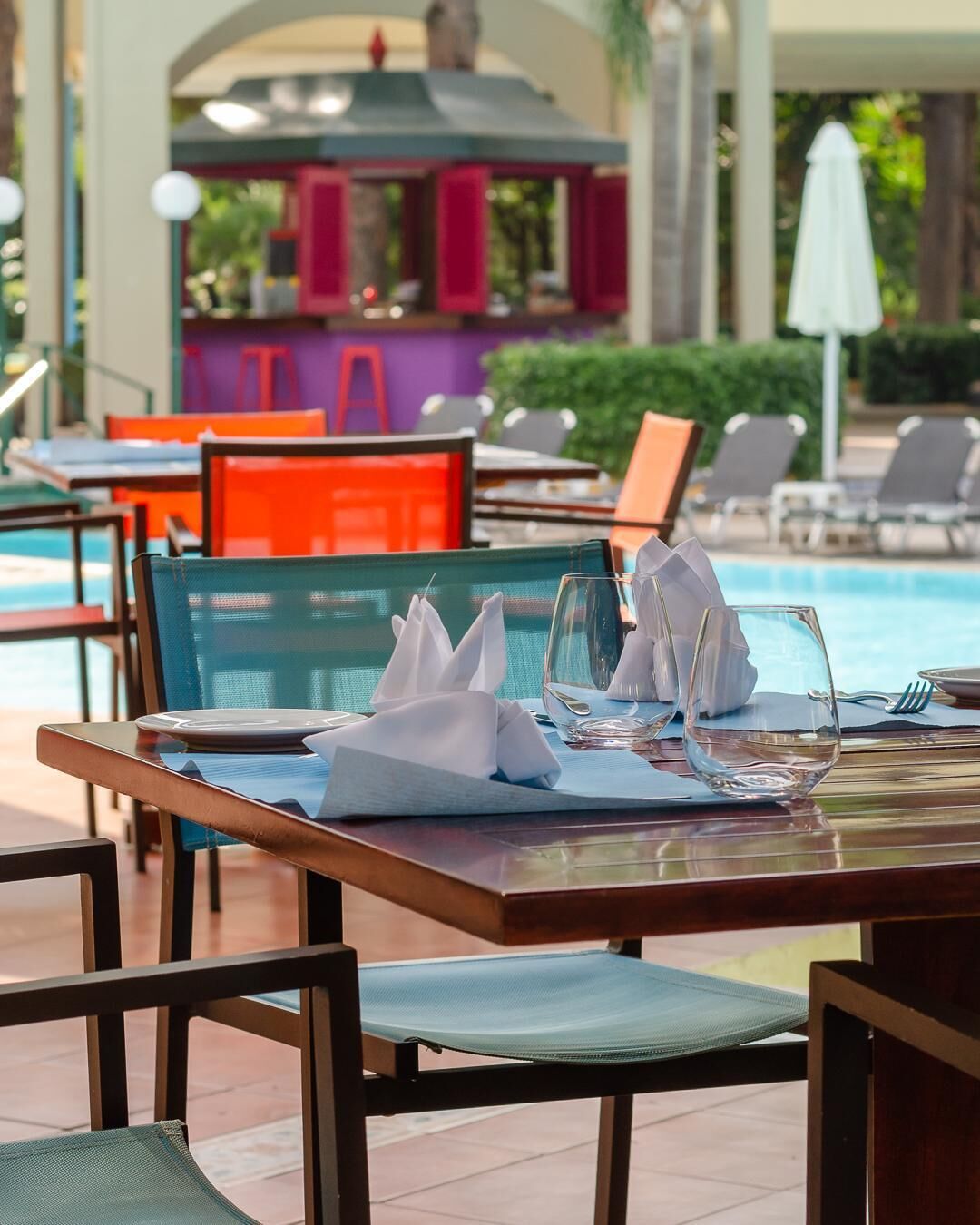 A dining area with tables set for two, near a poolside.