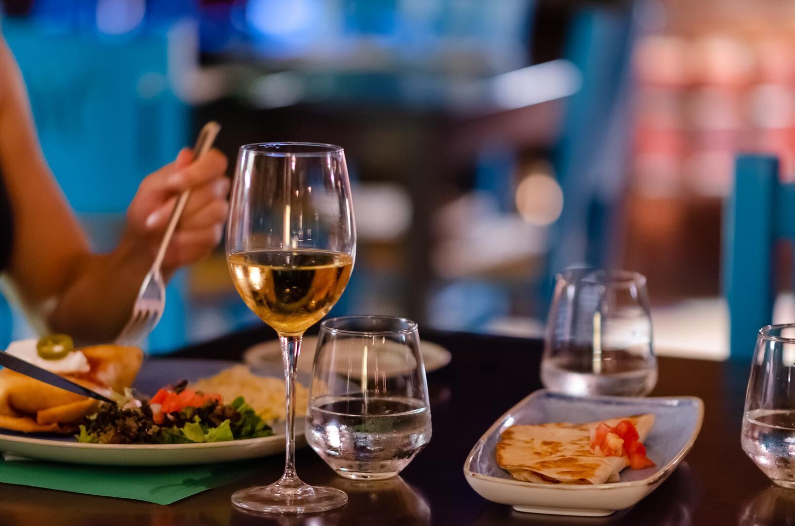 A dining table with a plate of food, a glass of white wine, and two water glasses.