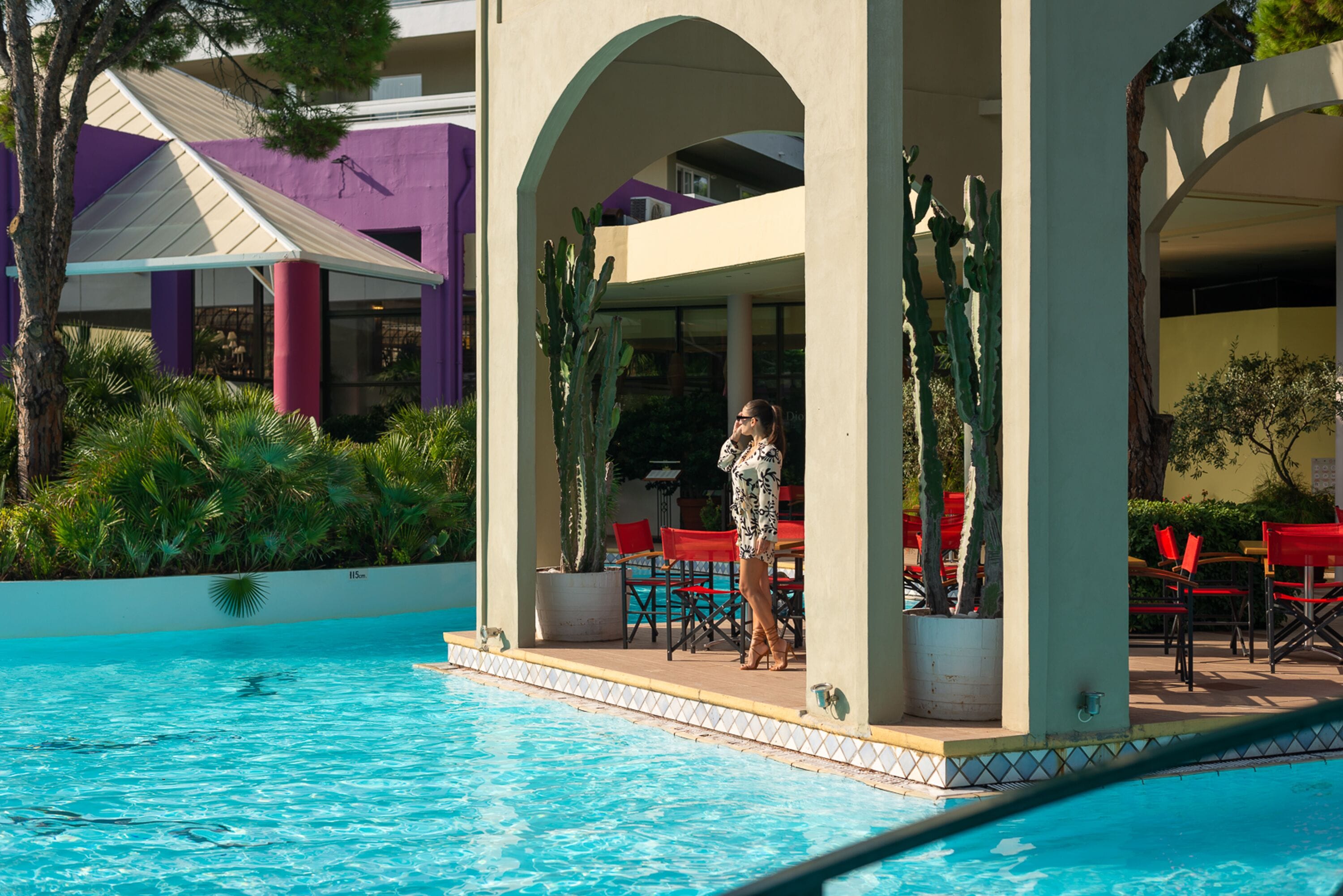 A pool area with a covered seating area, red chairs, and potted plants.