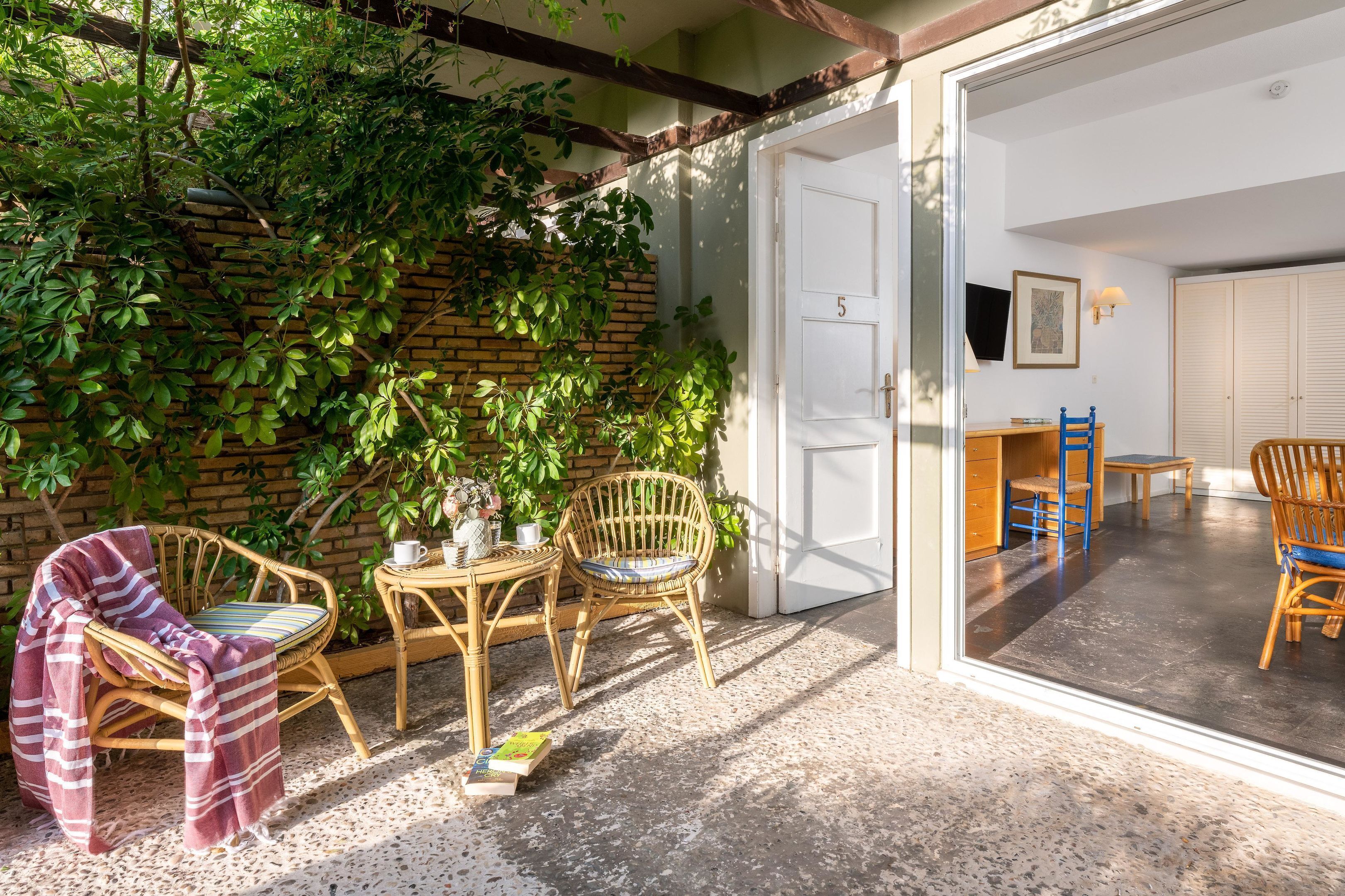 Un área de estar exterior acogedora con mobiliario de mimbre, un muro de ladrillo y una puerta que da a una habitación.