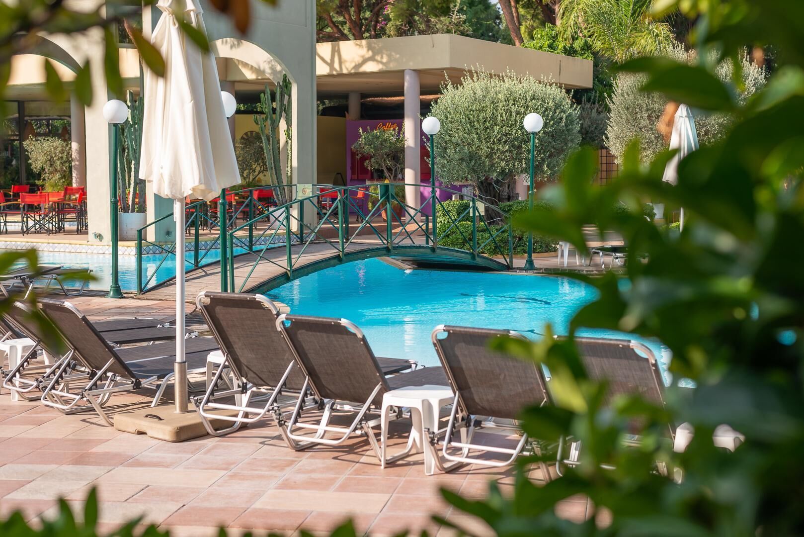 Zona de piscina con sillones de descanso y un pequeño puente sobre el agua.