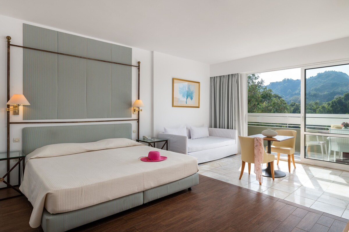 Habitación de hotel con cama, sofá, mesa de comedor y vistas al exterior.