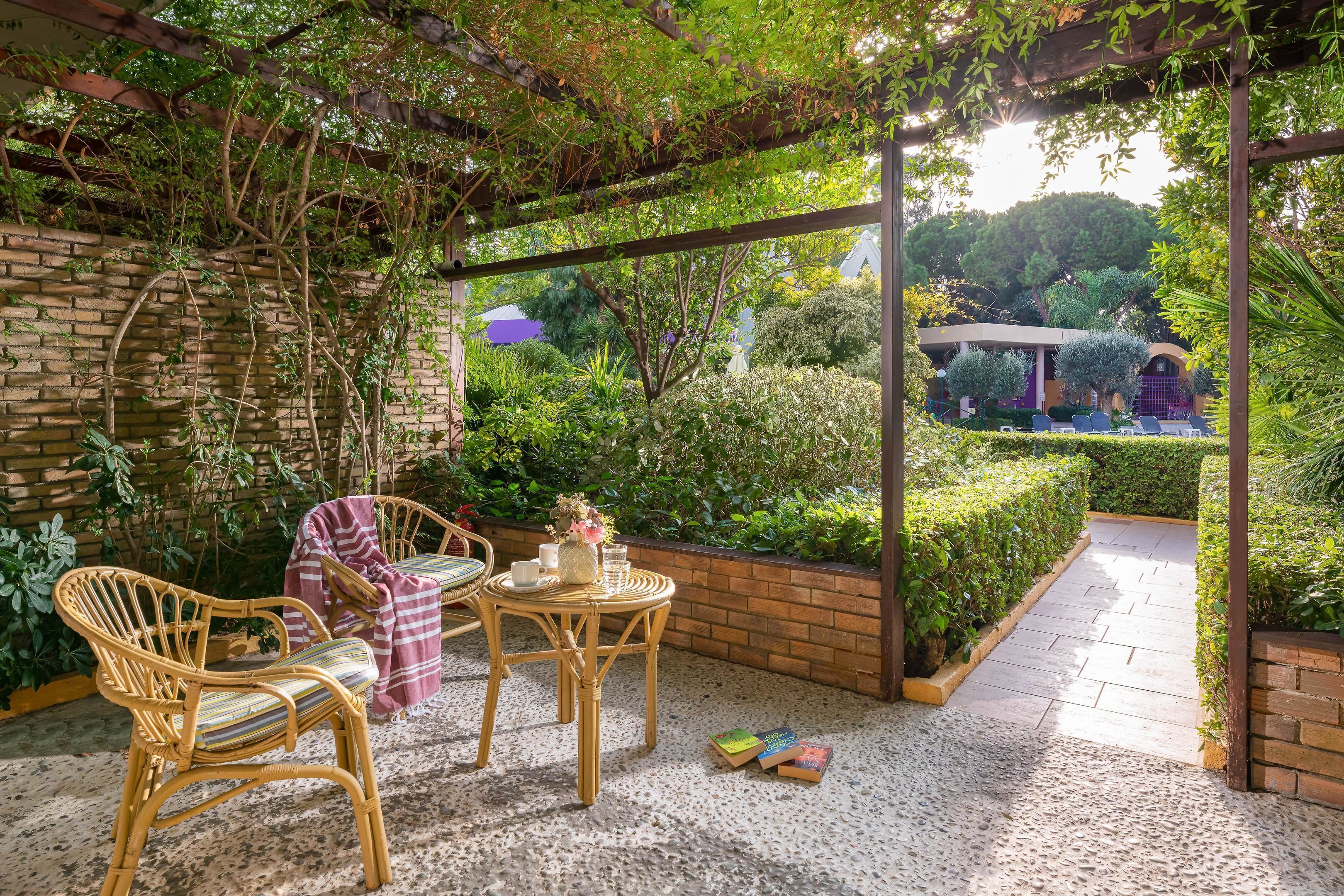 Un patio cubierto con mobiliario de mimbre, una mesa pequeña y un muro de ladrillo.